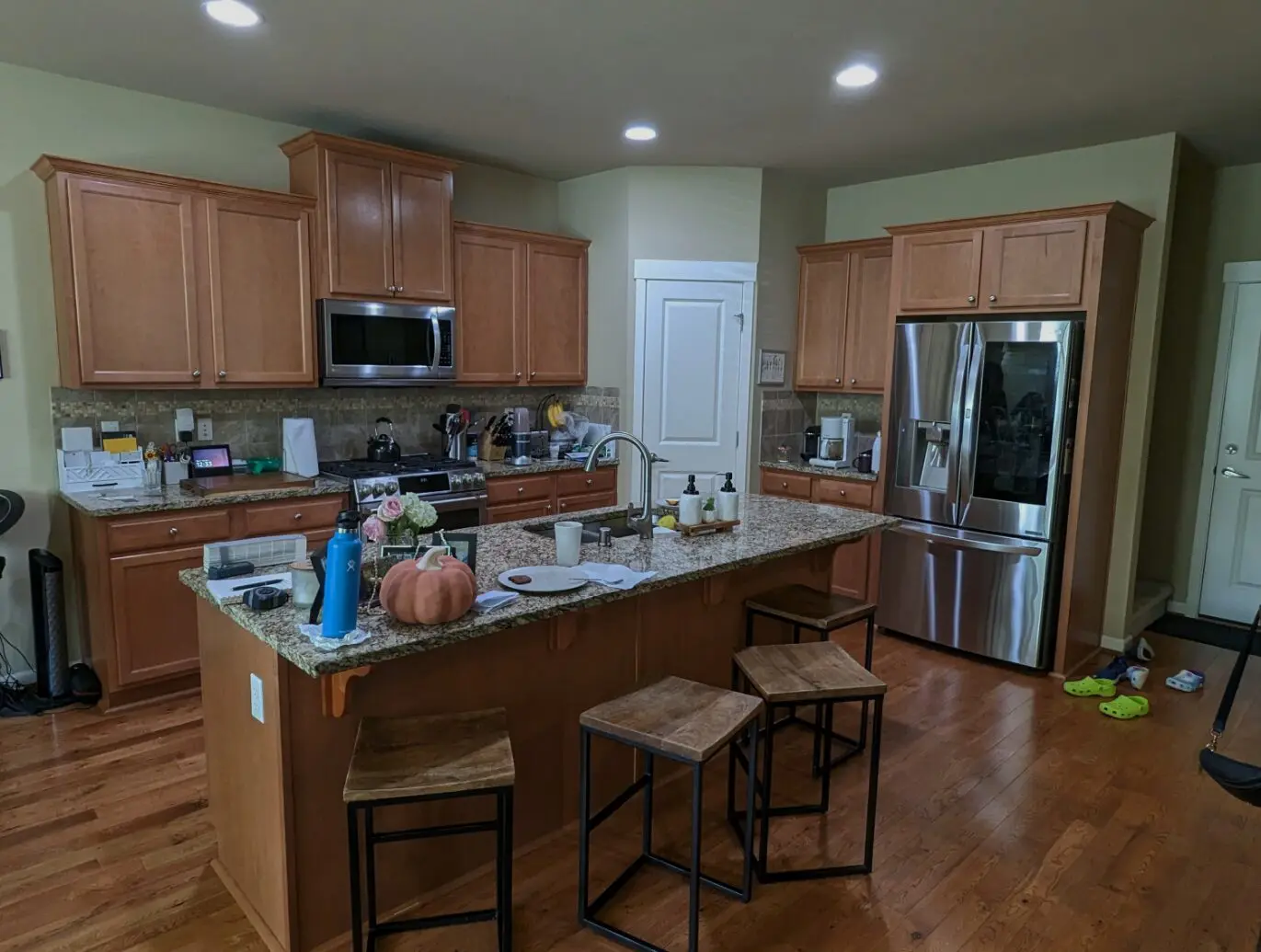 A modern kitchen by a transitional interior designer in Issaquah, WA, featuring wooden cabinets, a central island with stools, kitchen appliances, and items scattered on the counter.